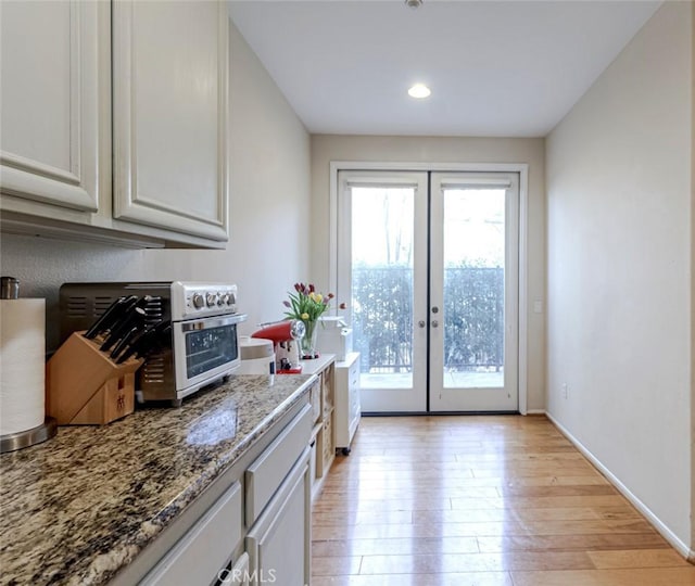 kitchen with french doors, light stone countertops, white cabinets, and light hardwood / wood-style flooring