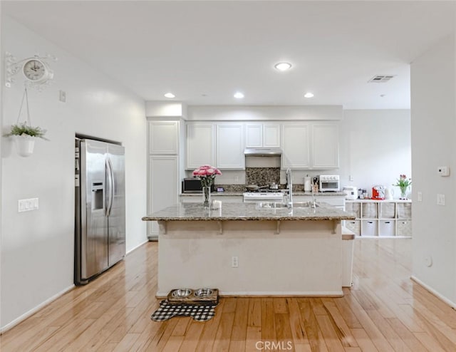 kitchen featuring a kitchen island with sink, stainless steel fridge with ice dispenser, light stone countertops, and white cabinets