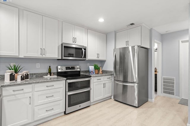 kitchen with stainless steel appliances, light stone countertops, light wood-type flooring, and white cabinets