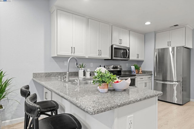 kitchen featuring sink, a breakfast bar, appliances with stainless steel finishes, white cabinetry, and kitchen peninsula