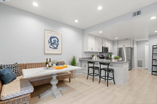 kitchen featuring appliances with stainless steel finishes, light stone countertops, light hardwood / wood-style flooring, and white cabinets