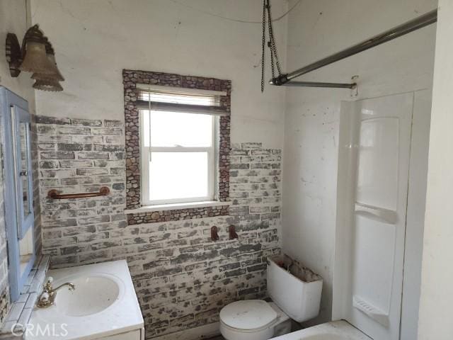 bathroom featuring brick wall, vanity, toilet, and a shower