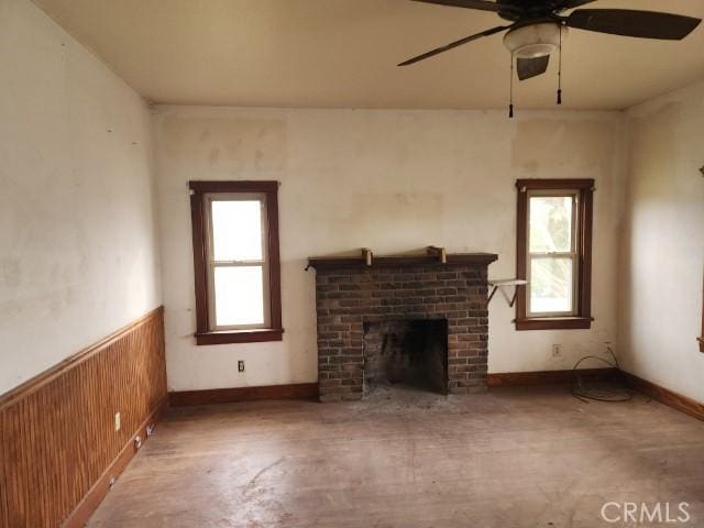 unfurnished living room featuring a fireplace, ceiling fan, wooden walls, and plenty of natural light