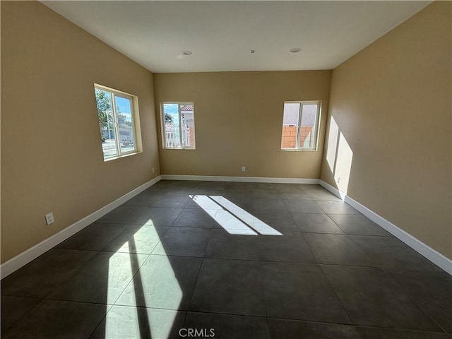 spare room with dark tile patterned floors and a healthy amount of sunlight