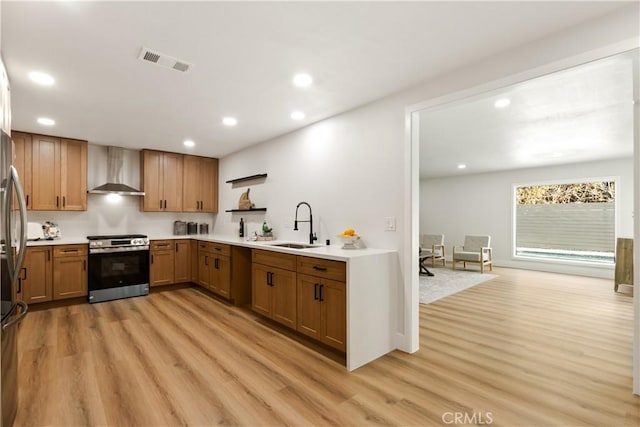 kitchen featuring light wood-type flooring, stainless steel range, sink, and wall chimney range hood