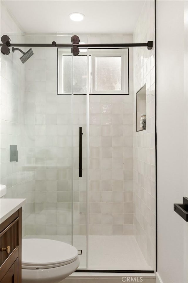 bathroom featuring a shower with door, vanity, and toilet