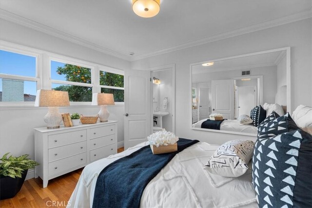 bedroom with visible vents, ensuite bathroom, crown molding, and wood finished floors