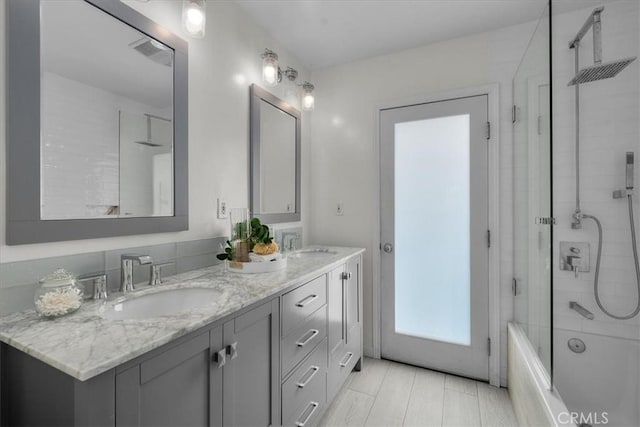 full bath featuring double vanity, visible vents, bath / shower combo with glass door, and a sink