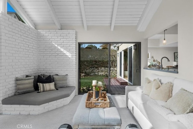 carpeted living room featuring brick wall, lofted ceiling with beams, and a sink