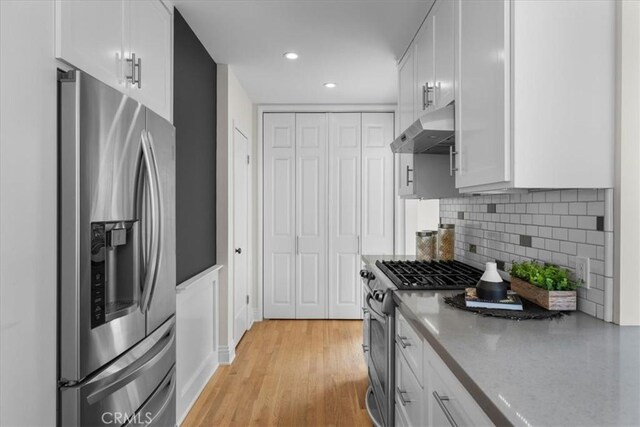 kitchen with under cabinet range hood, decorative backsplash, light wood-style flooring, stainless steel appliances, and white cabinetry