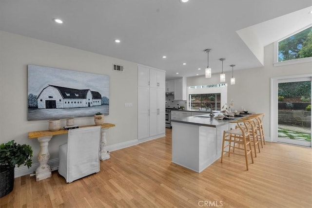 kitchen with a breakfast bar area, white cabinets, hanging light fixtures, stainless steel range, and light hardwood / wood-style floors