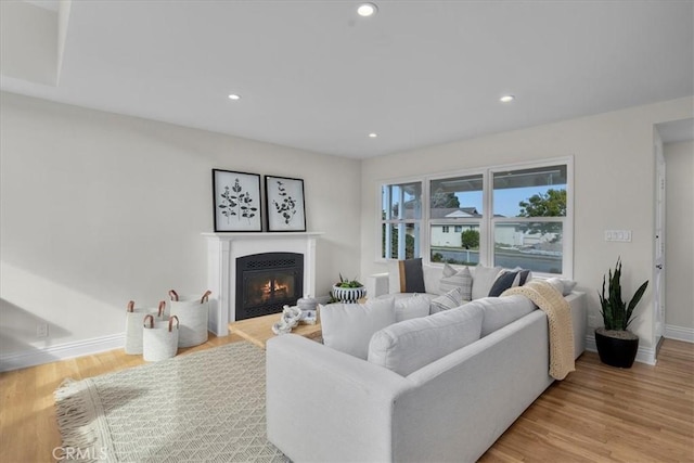 living area with a glass covered fireplace, recessed lighting, baseboards, and wood finished floors