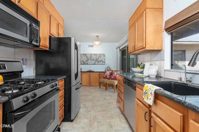 kitchen with tasteful backsplash, appliances with stainless steel finishes, sink, and dark stone counters