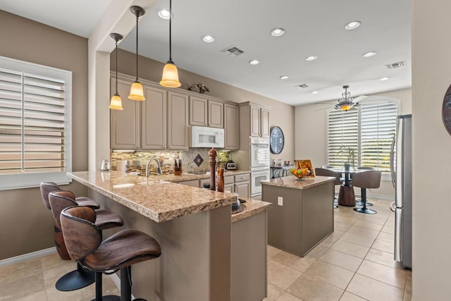 kitchen with a kitchen breakfast bar, hanging light fixtures, light stone counters, kitchen peninsula, and white appliances