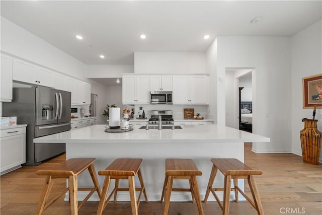 kitchen with stainless steel appliances, a breakfast bar, a center island with sink, and white cabinets