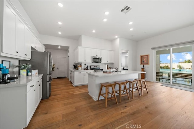 kitchen featuring a breakfast bar, white cabinets, a kitchen island with sink, light hardwood / wood-style floors, and stainless steel appliances