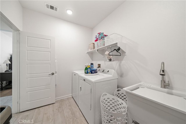 clothes washing area with light hardwood / wood-style floors, separate washer and dryer, and sink