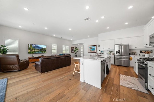 kitchen featuring sink, a breakfast bar area, a kitchen island with sink, stainless steel appliances, and white cabinets