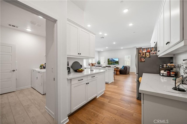 kitchen with white cabinetry, washer and clothes dryer, light stone counters, kitchen peninsula, and light wood-type flooring