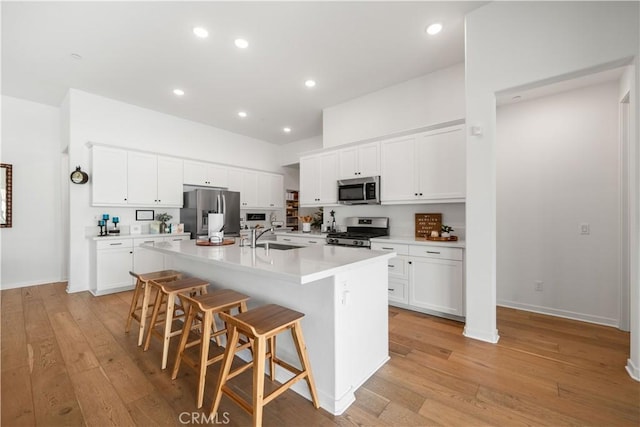 kitchen with a kitchen breakfast bar, an island with sink, white cabinets, and appliances with stainless steel finishes