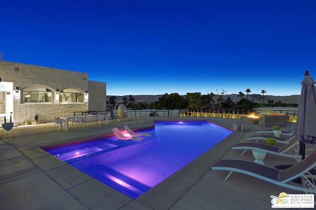 pool at dusk featuring a mountain view and a patio