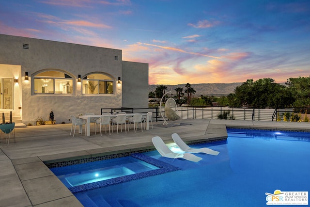 pool at dusk featuring an in ground hot tub, a mountain view, and a patio