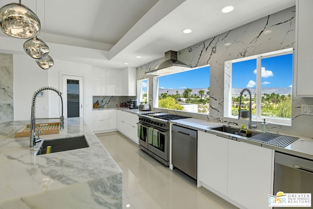 kitchen featuring sink, white cabinetry, hanging light fixtures, stainless steel appliances, and wall chimney range hood