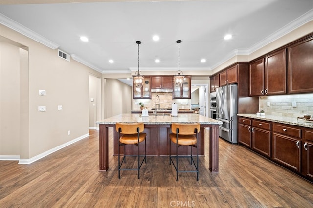 kitchen with an island with sink, light stone countertops, sink, and stainless steel fridge