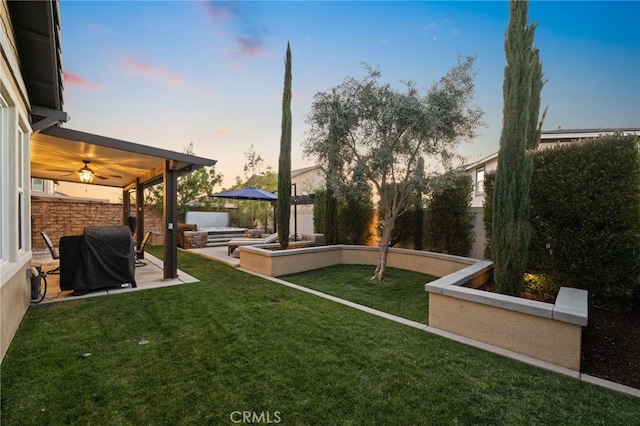 yard at dusk featuring ceiling fan and a patio area