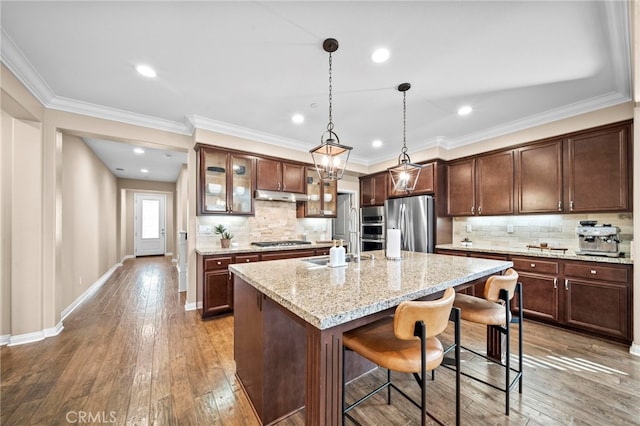 kitchen with light stone counters, a center island with sink, hardwood / wood-style flooring, pendant lighting, and stainless steel appliances