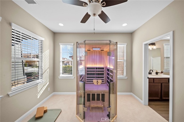 bedroom with ceiling fan, sink, light colored carpet, and ensuite bath