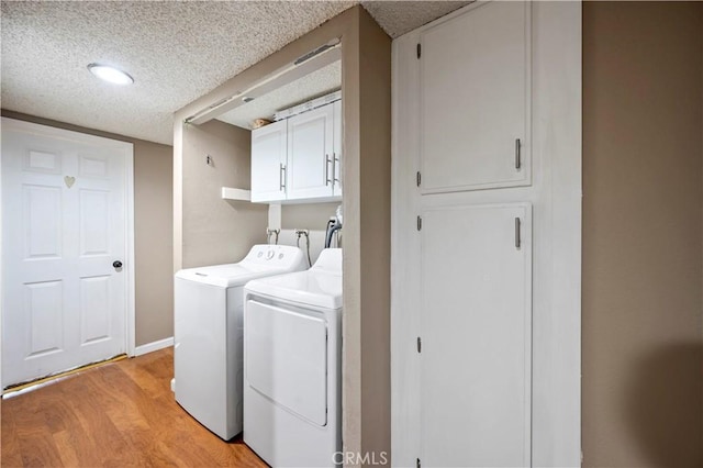 clothes washing area featuring cabinets, washing machine and dryer, light hardwood / wood-style flooring, and a textured ceiling