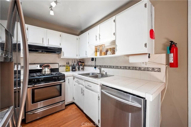 kitchen featuring sink, white cabinetry, tile countertops, appliances with stainless steel finishes, and backsplash