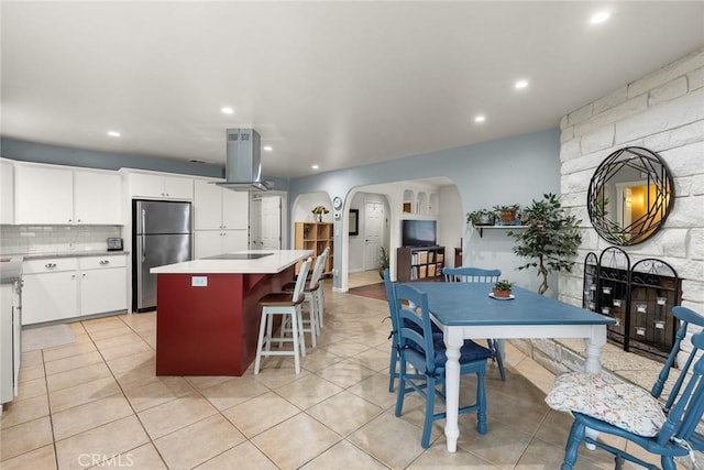 kitchen featuring light tile patterned flooring, white cabinetry, island range hood, a center island, and stainless steel fridge