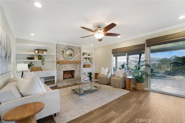 living room featuring built in features, a fireplace, ornamental molding, ceiling fan, and light hardwood / wood-style floors