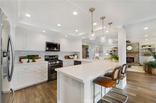 kitchen with a raised ceiling, white cabinetry, appliances with stainless steel finishes, and kitchen peninsula