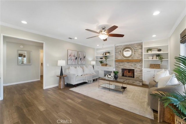 living room featuring built in features, a fireplace, ornamental molding, ceiling fan, and dark wood-type flooring