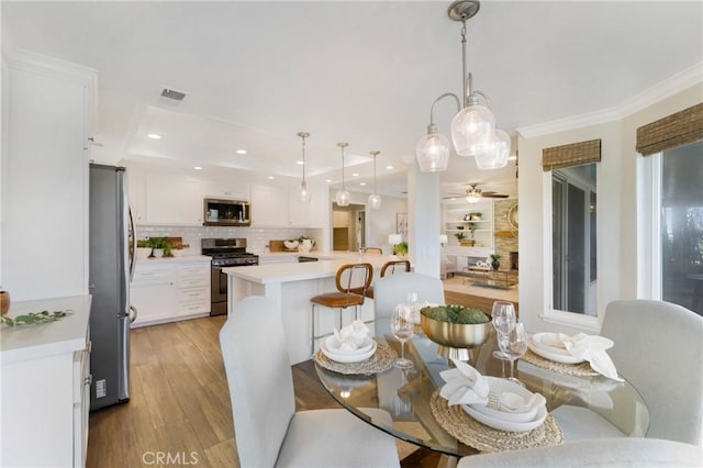 dining area featuring ceiling fan, ornamental molding, and light wood-type flooring