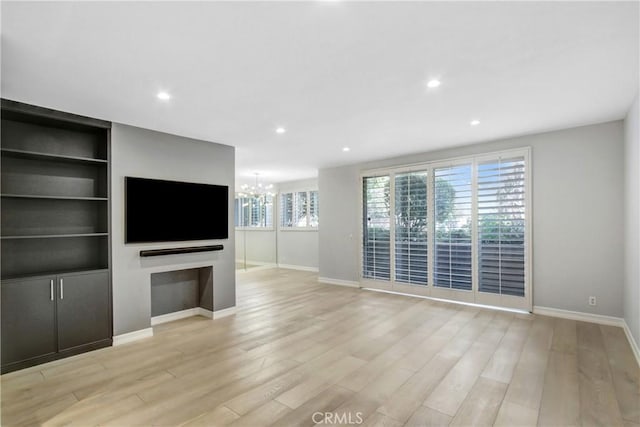 unfurnished living room featuring built in features, a notable chandelier, and light hardwood / wood-style floors