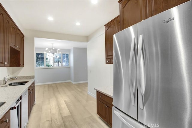 kitchen featuring sink, stainless steel appliances, light stone counters, light hardwood / wood-style floors, and decorative light fixtures