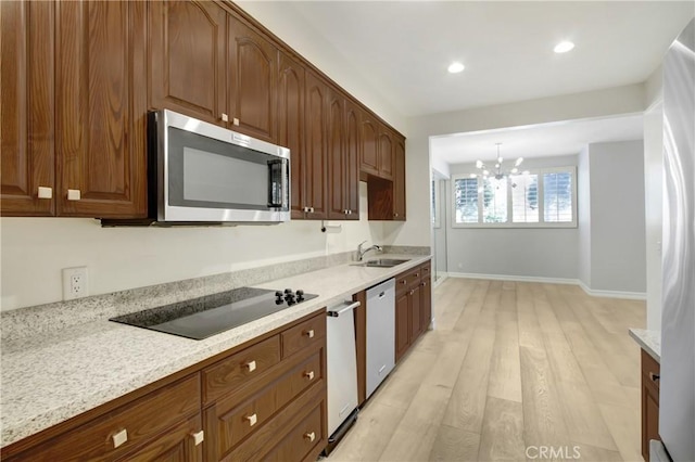 kitchen featuring sink, hanging light fixtures, light stone counters, stainless steel appliances, and light wood-type flooring