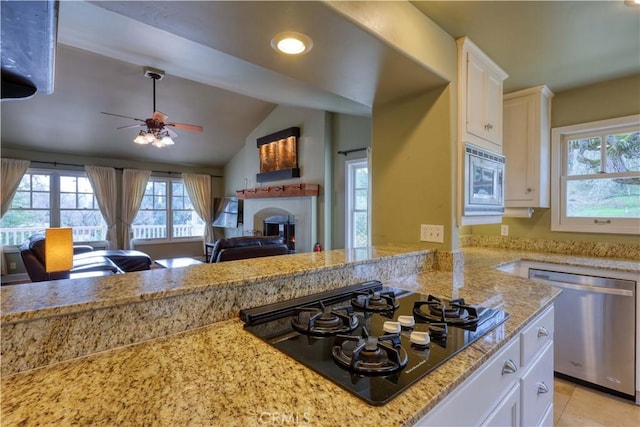 kitchen featuring appliances with stainless steel finishes, white cabinetry, light stone countertops, vaulted ceiling, and kitchen peninsula