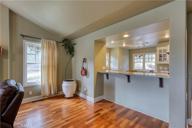 kitchen featuring a kitchen bar, white cabinetry, vaulted ceiling, hanging light fixtures, and kitchen peninsula