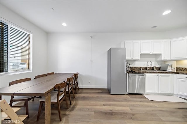 kitchen with sink, appliances with stainless steel finishes, dark stone countertops, white cabinetry, and light hardwood / wood-style floors