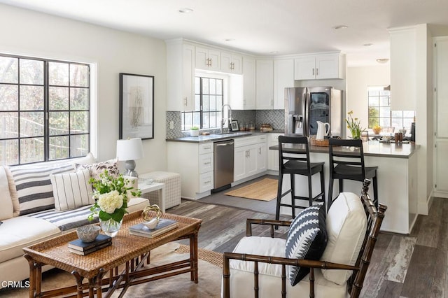 kitchen with appliances with stainless steel finishes, wood-type flooring, sink, white cabinets, and backsplash