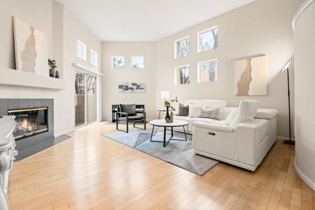 living room featuring a tiled fireplace, a high ceiling, and light wood-type flooring