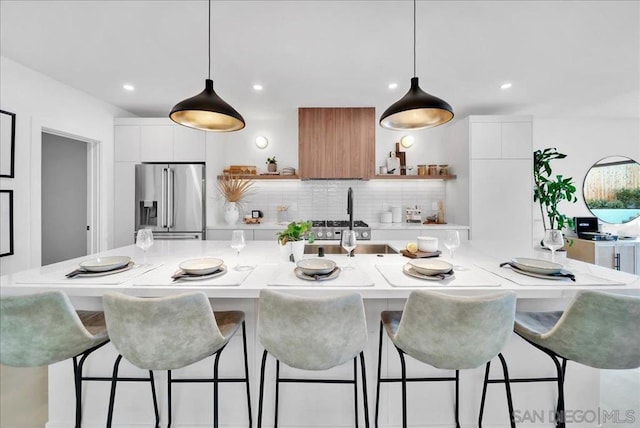 kitchen with white cabinetry, high quality fridge, and a center island with sink