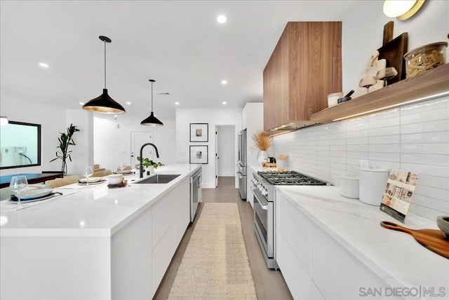 kitchen featuring decorative light fixtures, an island with sink, sink, white cabinets, and premium appliances