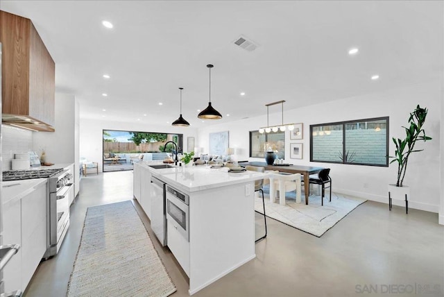 kitchen featuring appliances with stainless steel finishes, a kitchen breakfast bar, pendant lighting, a kitchen island with sink, and white cabinets