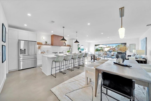 kitchen featuring tasteful backsplash, an island with sink, white cabinetry, hanging light fixtures, and high end fridge